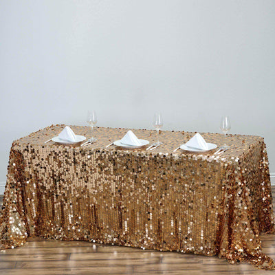Gold sequin tablecloth draped over a dining table with white napkins and glasses.