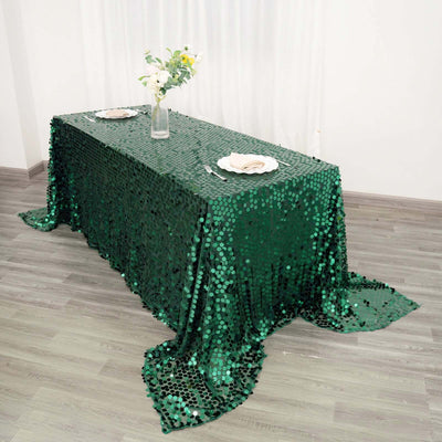 Green sequin tablecloth draped over a table with decorative plates and flowers.
