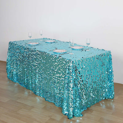 Turquoise sequin tablecloth draped over a table, set for dining.