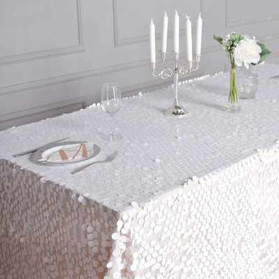 Elegant white sequin tablecloth draped over a dining table with candles and flowers.