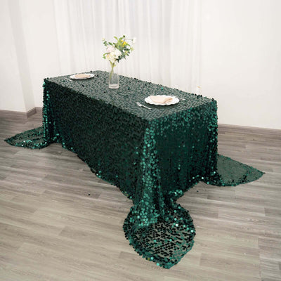 Green sequin tablecloth draped over a table with flower centerpiece and plates.