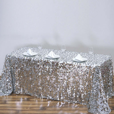 Sequin tablecloth in silver on a dining table with white plates and glasses.