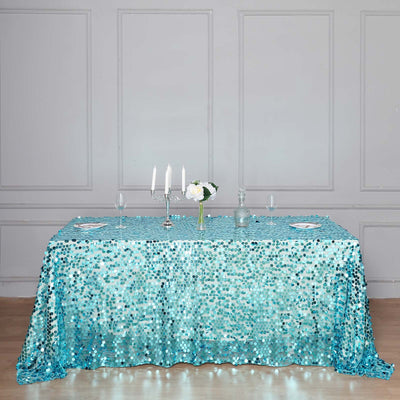 Turquoise sequin tablecloth draped over a dining table with candles and flowers.