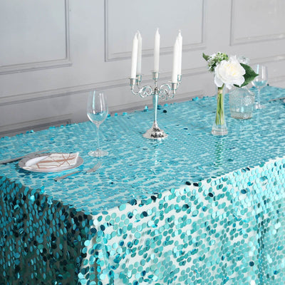Turquoise sequin tablecloth on elegantly set dining table with candles and flowers.