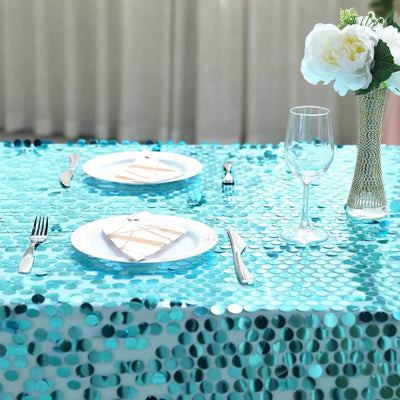 Turquoise sequin tablecloth with plates and glassware for elegant dining setup.