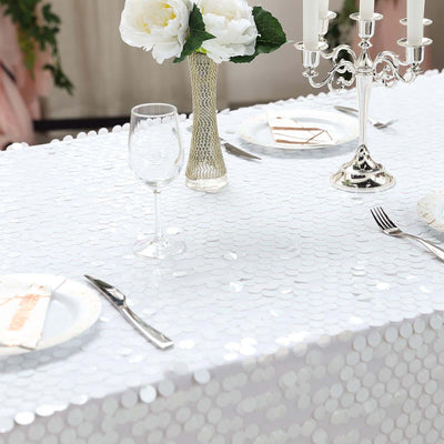 Elegant table setting with sequined white tablecloth, glassware, and floral centerpiece.