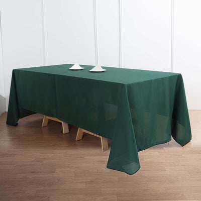 Green tablecloth draped over a wooden table with two white plates on top.