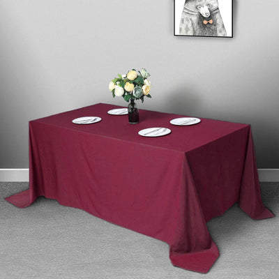 Burgundy tablecloth draped over a dining table with plates and a vase of flowers.