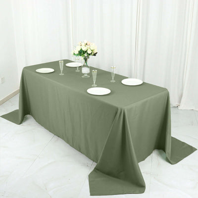Olive green tablecloth draped on a dining table with floral centerpiece and dinnerware.