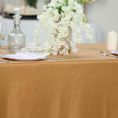 Elegant table setting with gold tablecloth, glassware, and floral centerpiece.