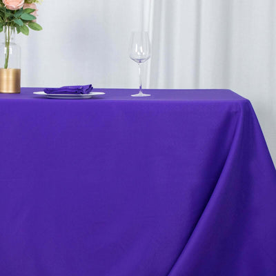 Purple tablecloth draped over a table set with a glass and plate.