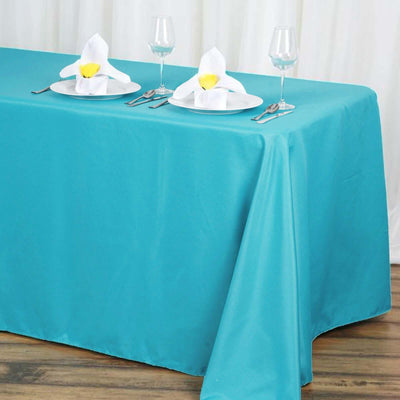 Turquoise tablecloth draped over a table set for dining with plates and glasses.