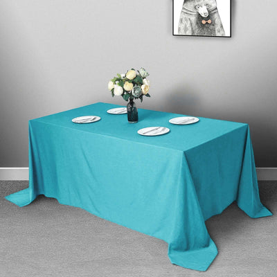 Turquoise tablecloth draped on a table with plates and a flower vase.