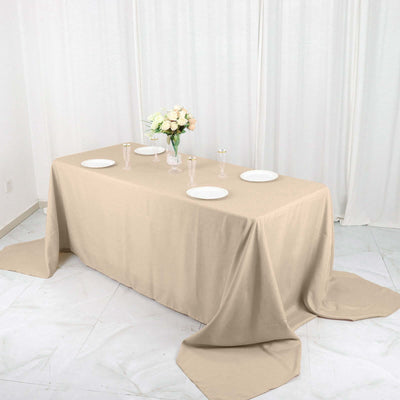 Beige tablecloth draped over a table set with plates and a vase of flowers.