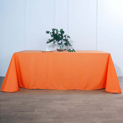 Orange tablecloth draped over a table with a vase of flowers.
