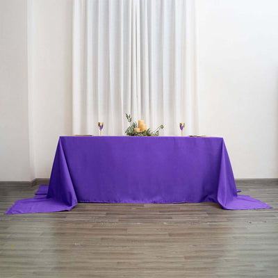Purple tablecloth draped elegantly over a table with candles and greenery.