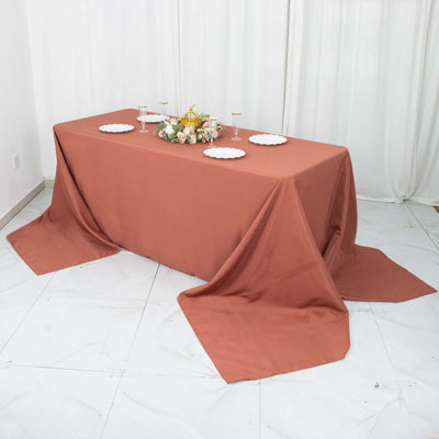 Rust-colored tablecloth draped over a table set with plates and floral centerpiece.