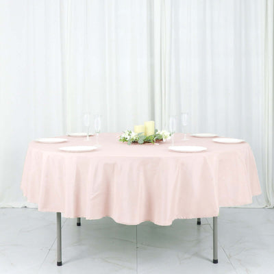 Round pink tablecloth draped over a table with plates and candles on a white backdrop.