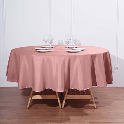 Round pink tablecloth draped over a wooden table set with plates and glasses.