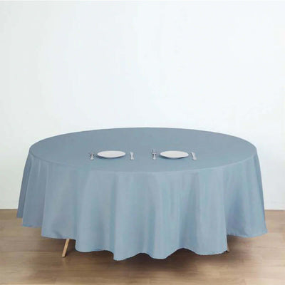 Round blue tablecloth on a wooden table with plates and cutlery