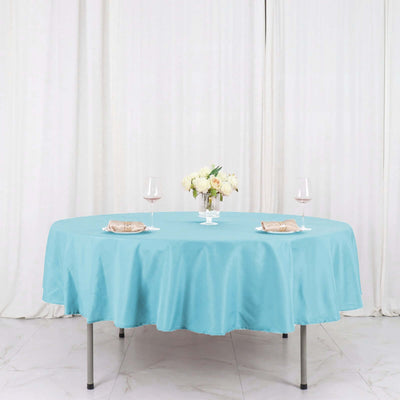 Round turquoise tablecloth on a dining table with floral centerpiece and wine glasses.