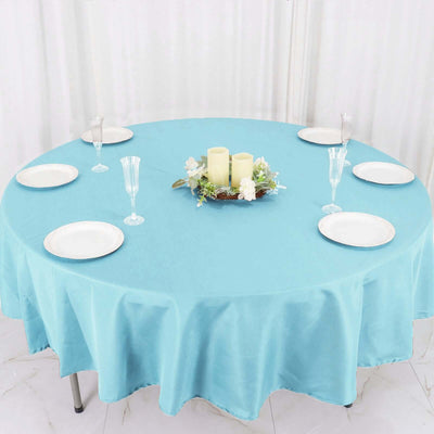 Round turquoise tablecloth set for dining with plates and candles.