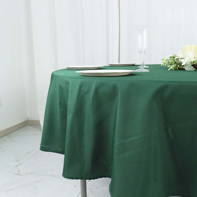 Green tablecloth draped over a round table set for a meal with plates and glassware.