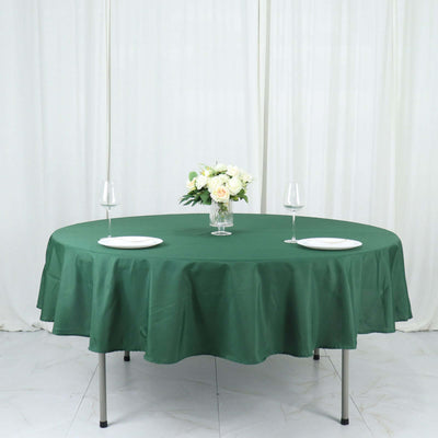 Round green tablecloth on a dining table with plates and glasses.