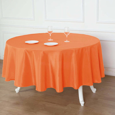 Round orange tablecloth draping over a table with plates and glasses.