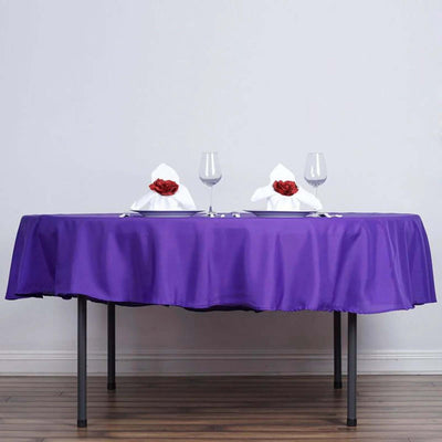 Purple tablecloth set for dinner with napkins and glasses.