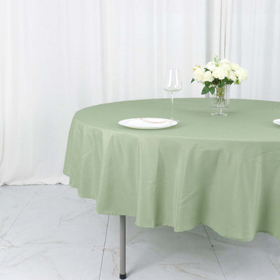 Round green tablecloth draped elegantly on a table with plates and flowers.