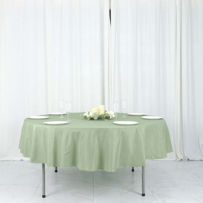 Round green tablecloth on a table set for dining with plates and decor.