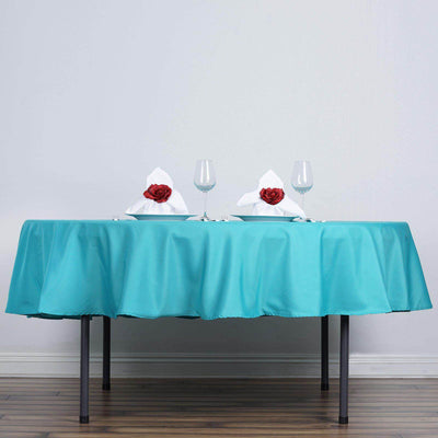 Elegant table setting with turquoise tablecloth and rose-adorned napkins.
