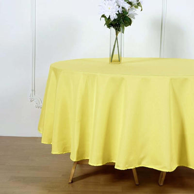 Yellow tablecloth draped over a round table with a vase of flowers.