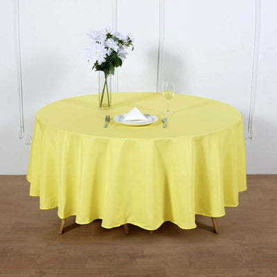 Yellow round tablecloth on a dining table with a vase and glass.