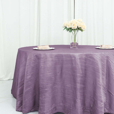 Purple textured tablecloth on a round table with a vase of roses.
