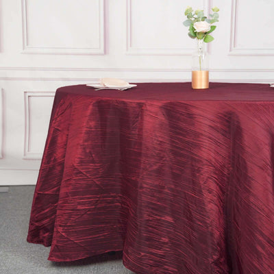 Burgundy tablecloth draped on a round table with a vase and flowers.