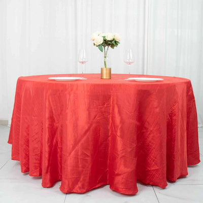 Round red tablecloth with floral centerpiece and wine glasses.
