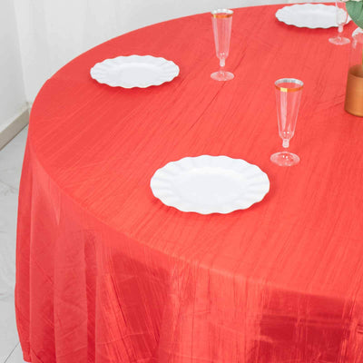 Red tablecloth on a round table with white plates and glasses.