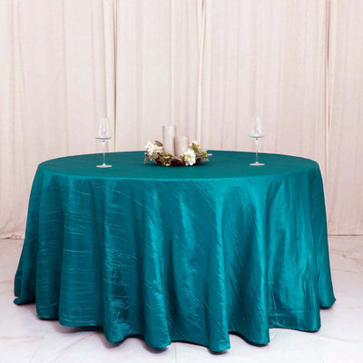 Teal tablecloth draped over a round table with decorative candles and glasses.