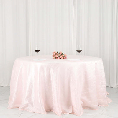 Elegant round table set with a pink tablecloth, flowers, and wine glasses.