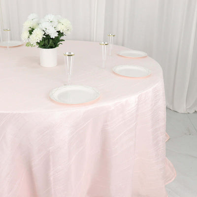 Elegant pink tablecloth draping over a round table with white plates and floral centerpiece.