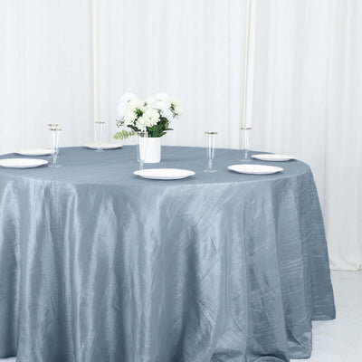 Round blue tablecloth draped over a table with plates and a floral centerpiece.