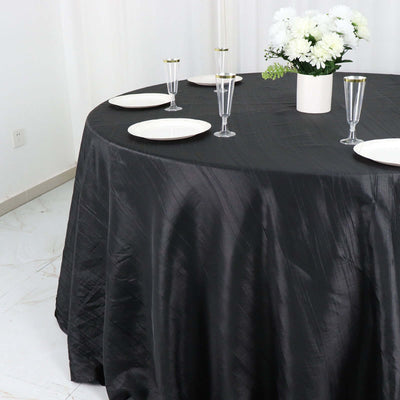 Black tablecloth draped over round table set for dining with plates and glasses.