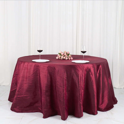 Round burgundy tablecloth on a table with wine glasses and floral centerpiece.