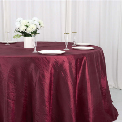 Burgundy tablecloth draped over a round table with white plates and floral centerpiece.