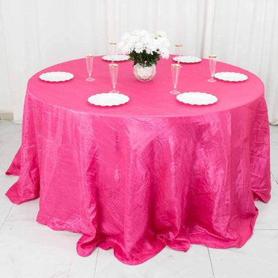 Pink tablecloth draped over a round table set with plates and glasses.