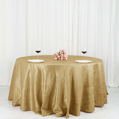 Elegant gold tablecloth draped over a round table with wine glasses and flowers.