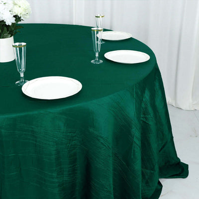 Green tablecloth on a round table set with white plates and glasses.