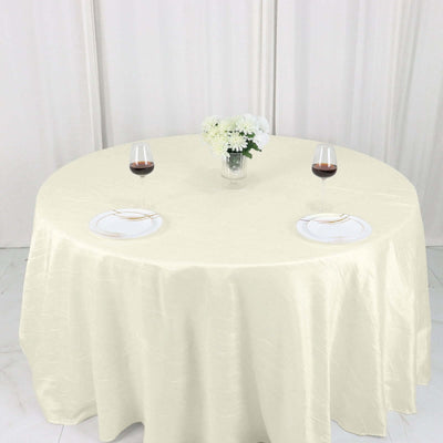Elegant round table set with wine glasses and plates on a cream tablecloth.
